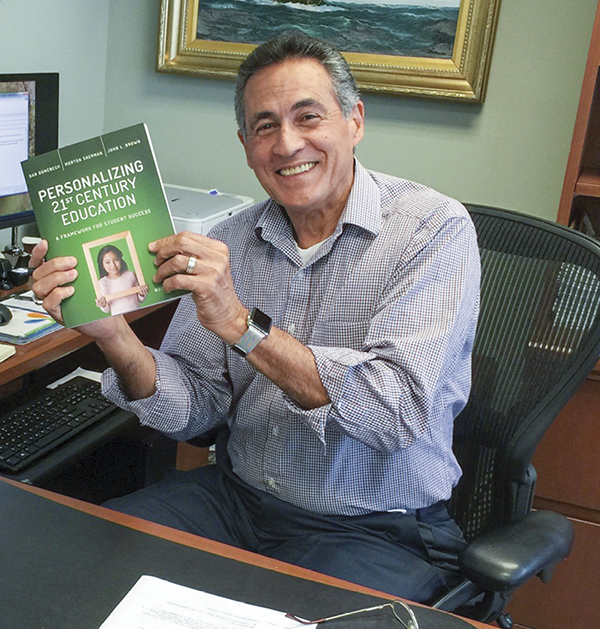 Dan Domenech holding his book sitting at desk