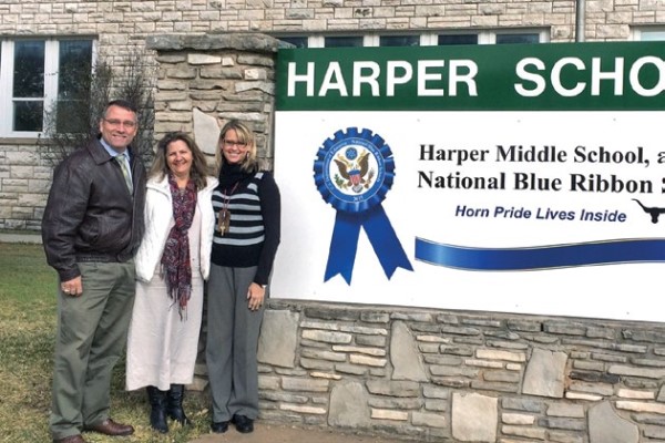 Chris Stevenson poses with two colleagues in front of the Harper Middle School sign