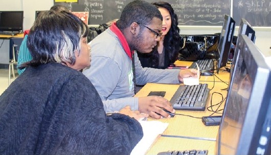 An adult assists a student at the computer with financial aid questions