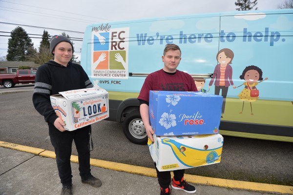 Two students carry boxes of produce from a Resource Center bus