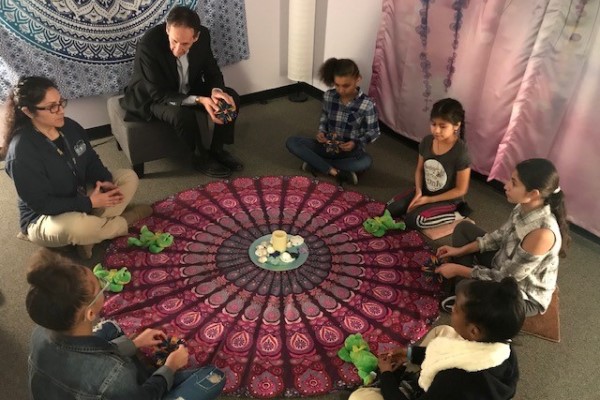 Students sit in a circle around a colorful rug