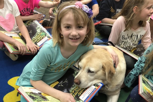 Therapy dog snuggles with a student while they read