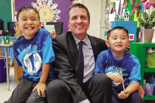 Corey Golla smiles for the camera with two young students