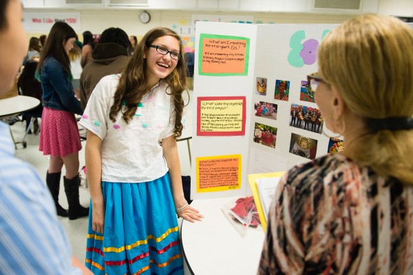 A student smiles and stands in front of a tri-fold presentation board