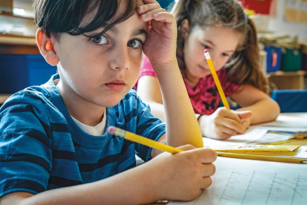 A child in a blue shirt looks at the camera while holding a pencil