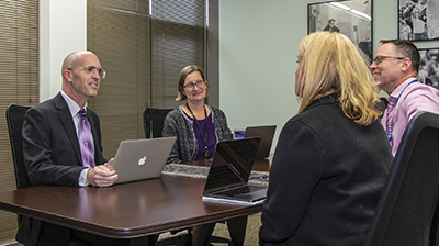 Two men and two women sitting at conference table with laptops