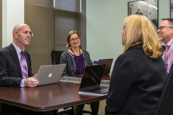 two men and two women at conference table with laptops