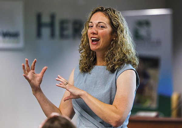 Rebecca Coffman talking and smiling, gesturing with hands and wearing gray dress