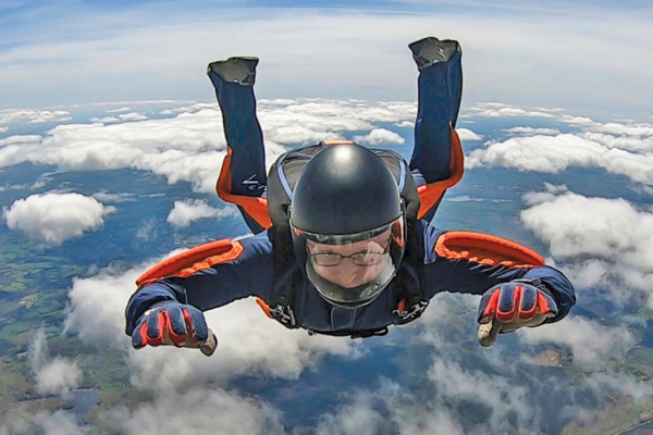 Oscar Sheikl mid-fall during skydiving. Clouds and blue sky surround him