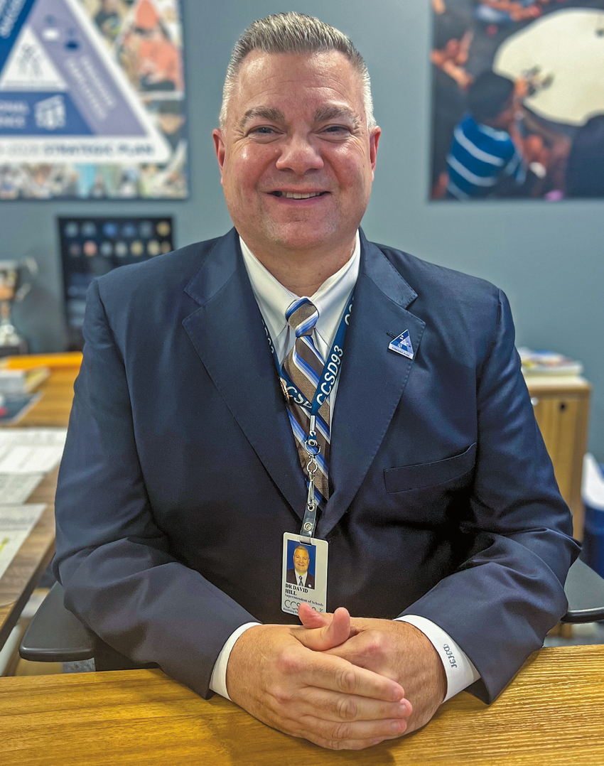 A man with short gray hair smiling in a blue suit