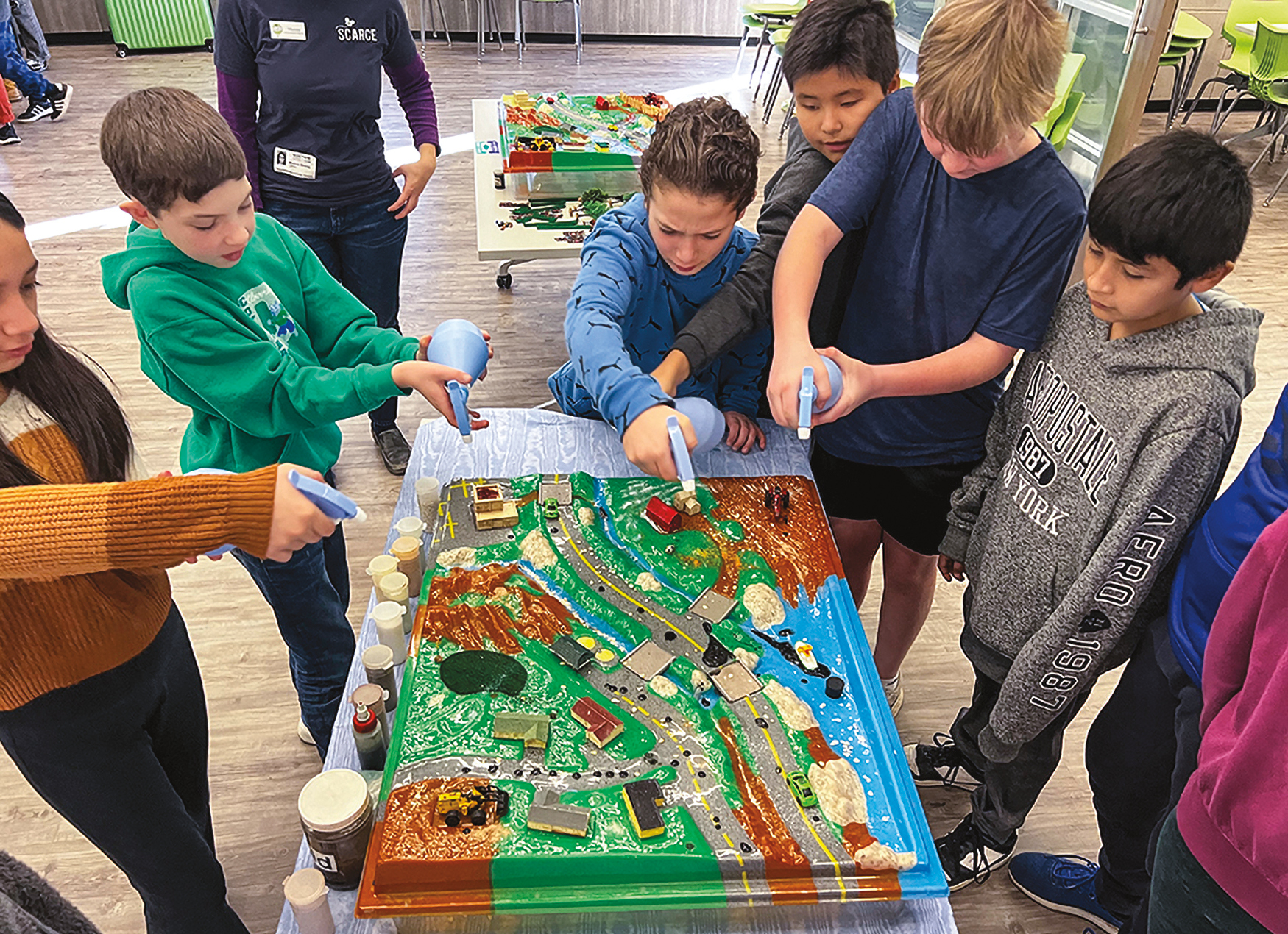 A group of children with a science or art project with roads and trees and cars