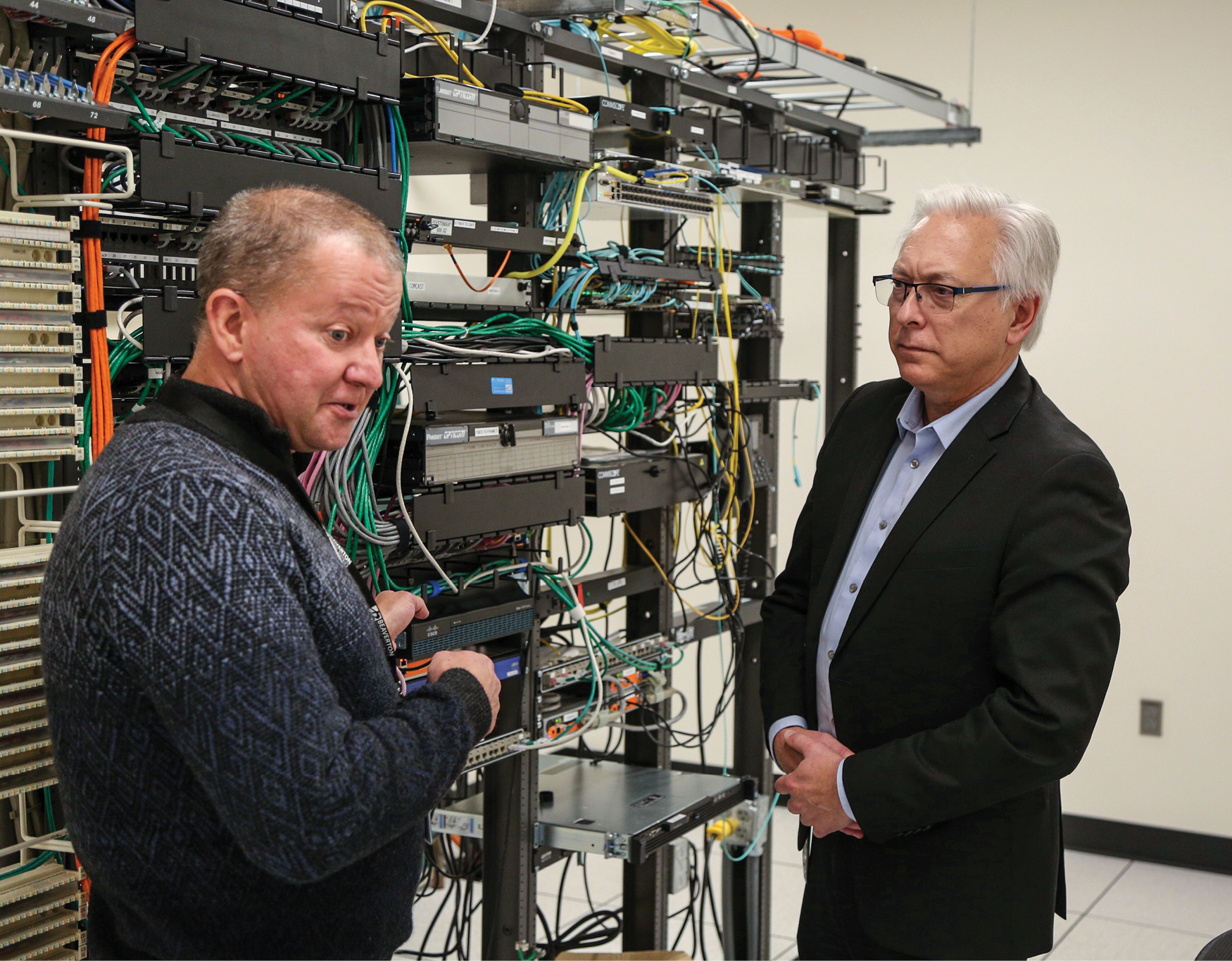 Two men standing in front of computer processing hardware. Man on right is Steve Langford, with gray hair wearing a black suit