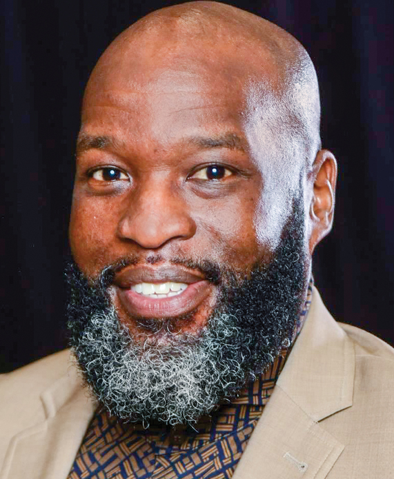 A Black man with a gray and black beard wearing a tan suit jacket