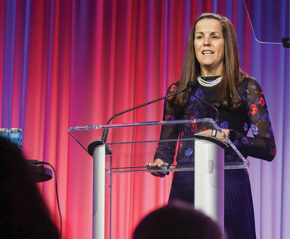 Noelle Ellerson Ng speaks at a glass podium in front of a colored light background