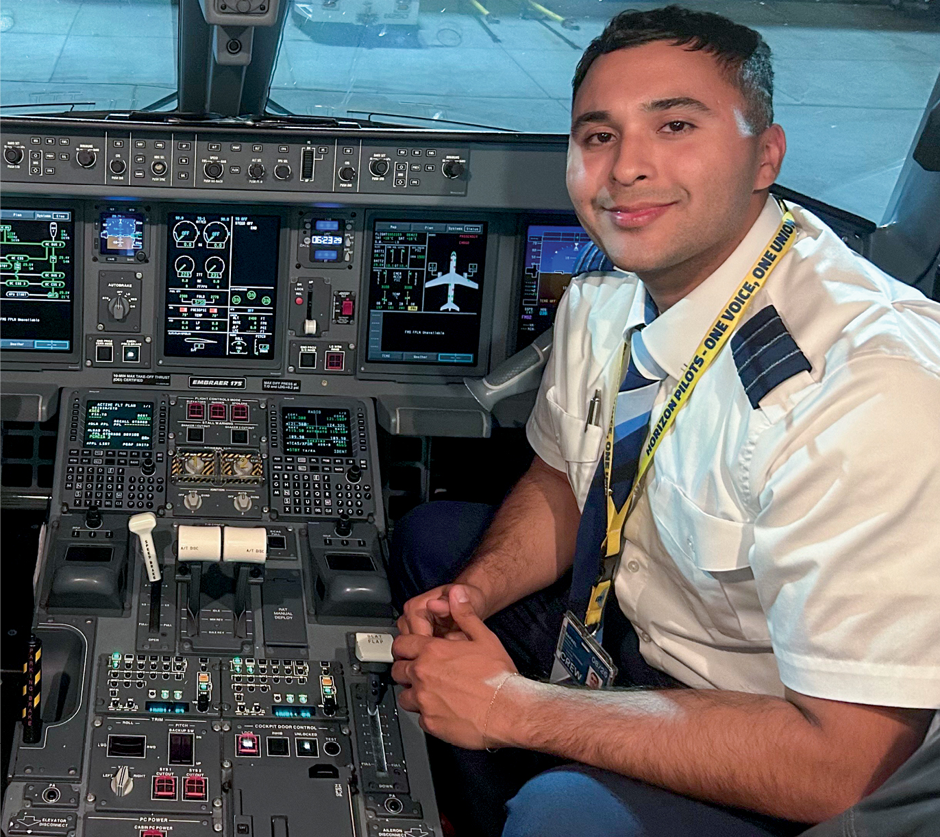 A teenager in a plane's cockpit smiling in a pilot uniform