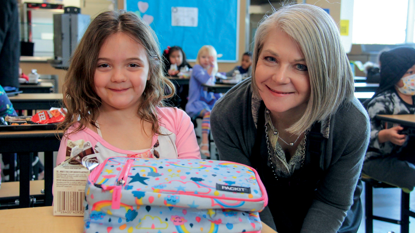 A white woman with gray hair smiling with a child at a desk