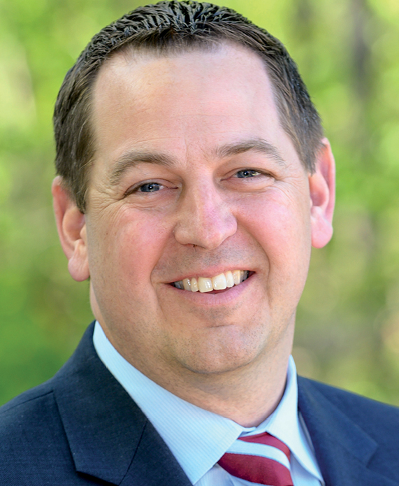 Josh Swanson headshot, a white man smiling wearing a suit