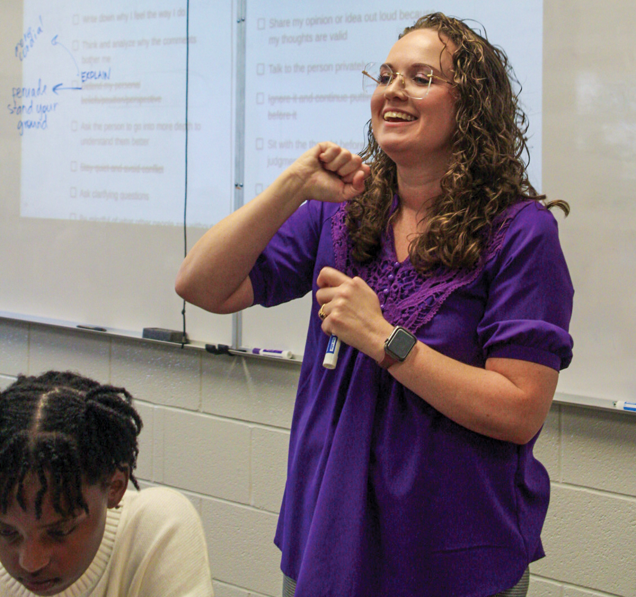 A woman in a purple shirt teaching at the front of a classroom