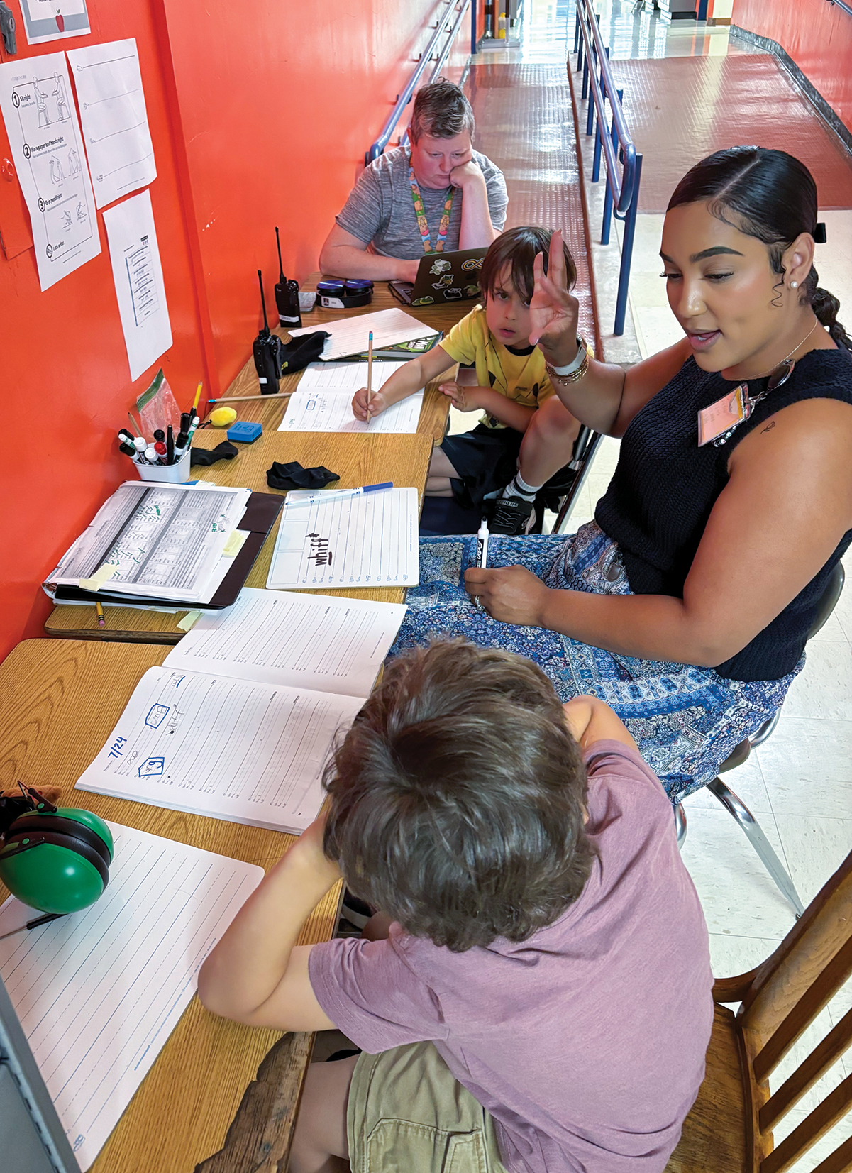 Woman tutoring two young students at a long table