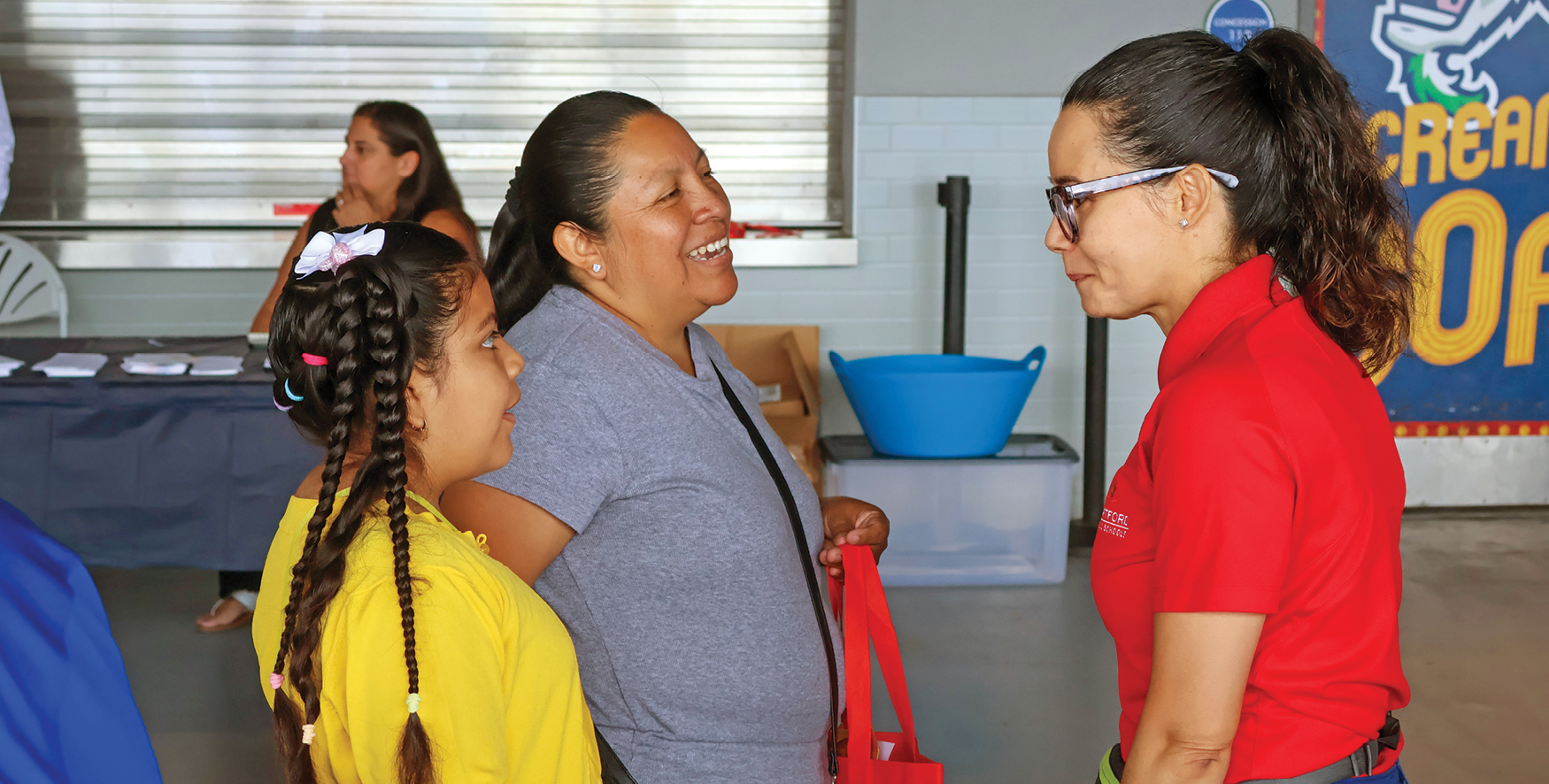 A woman in a red polo shirt talking to a mother and her daughter