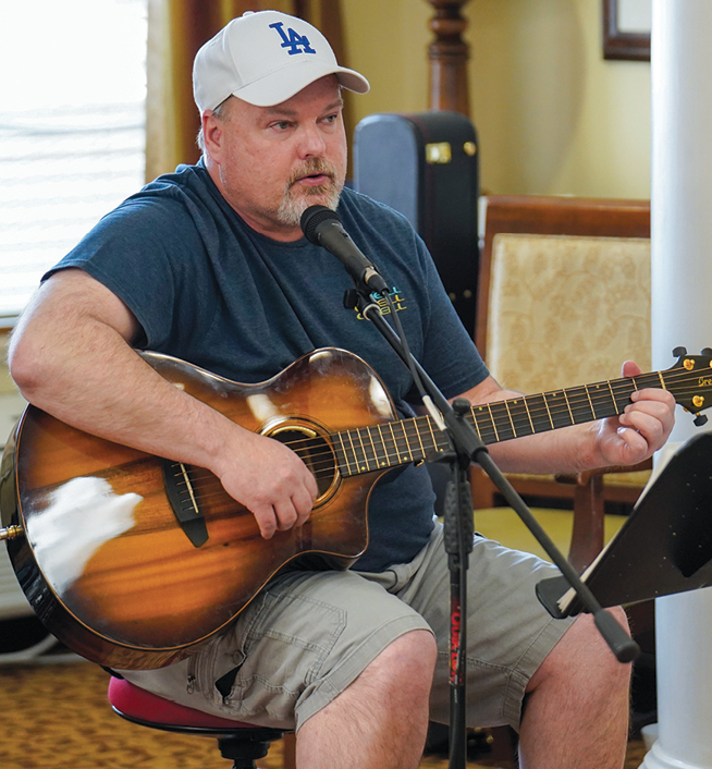 A man sitting at a microphone playing guitar with a music stand