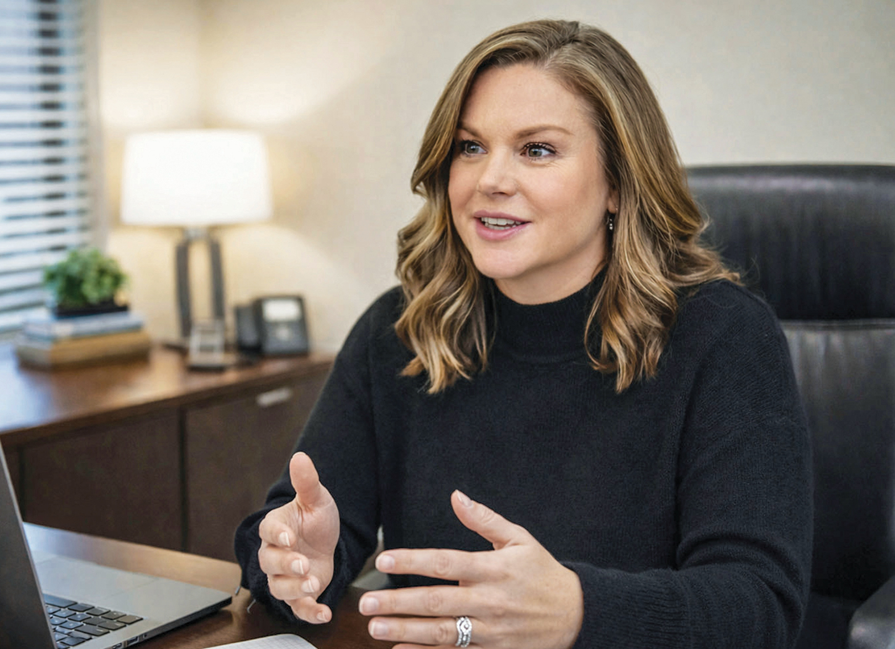 A brunette white woman in a black shirt talking sitting in her office chair