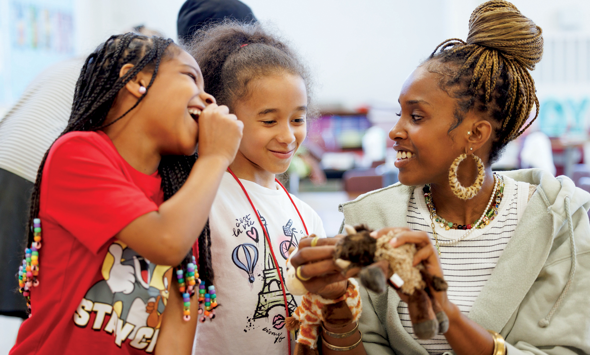 A Black woman smiles while working with two elementary aged children
