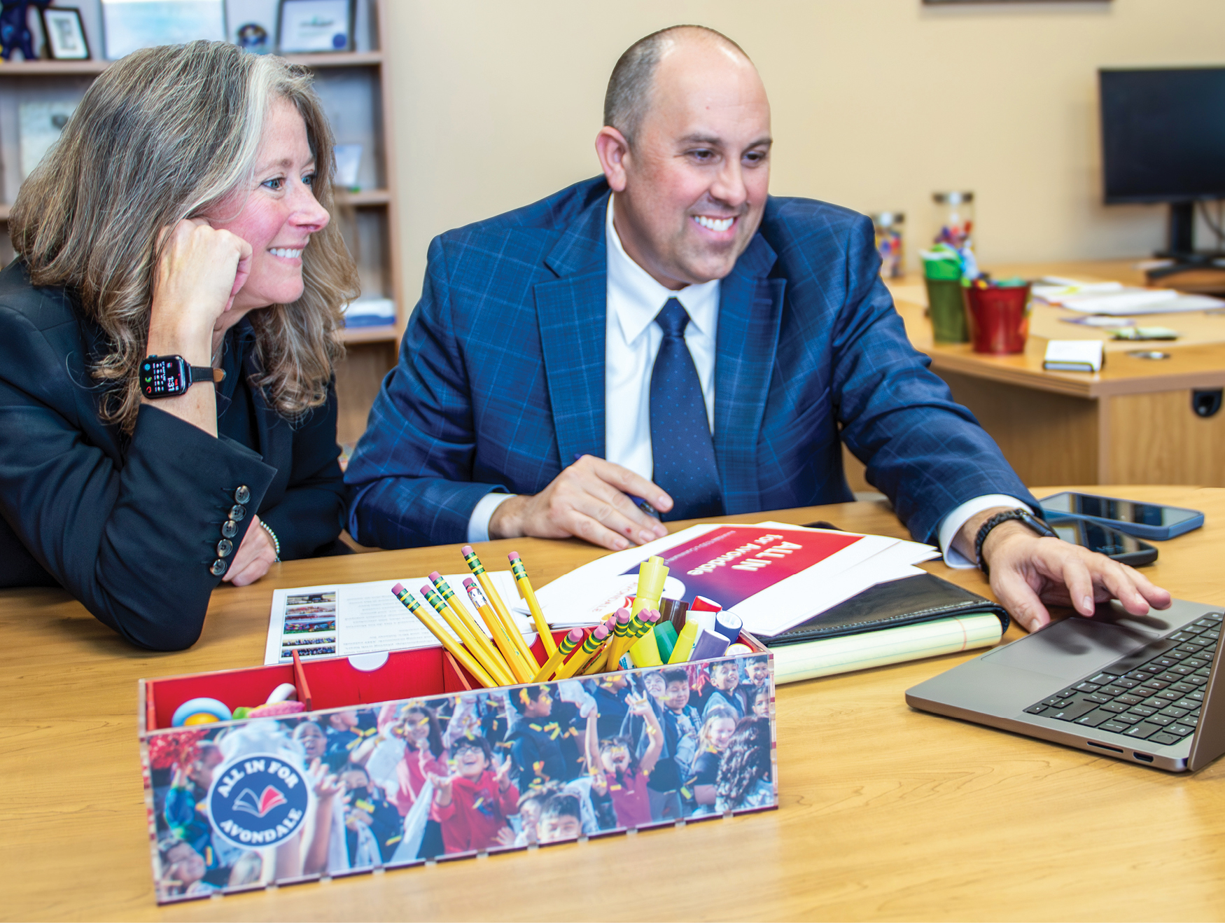 A woman and man sitting at a table smiling looking at laptop