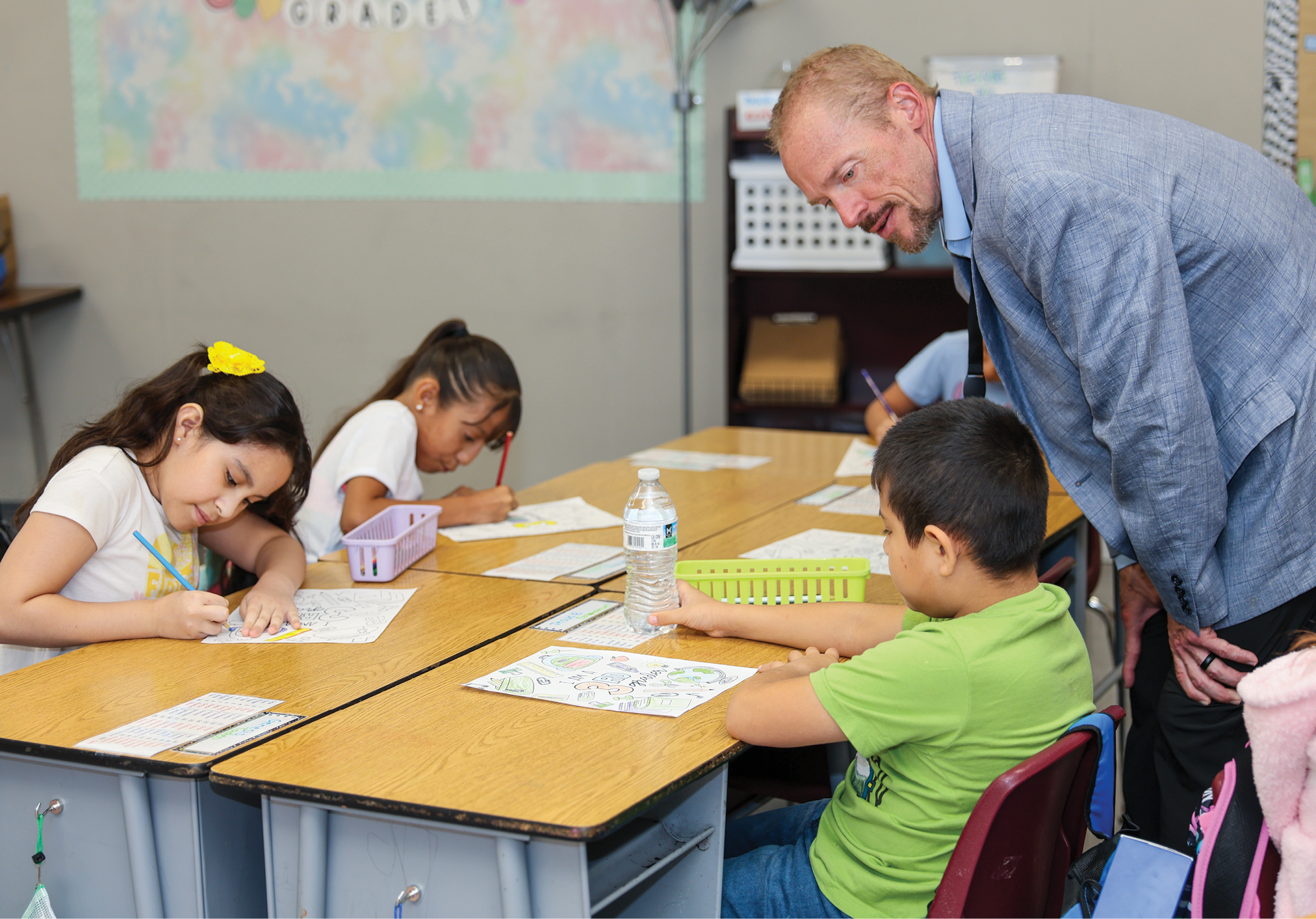 Man standing at desks talking to elementary school students