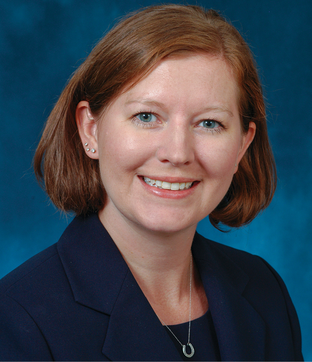 A headshot of a woman with red hair wearing a blue suit