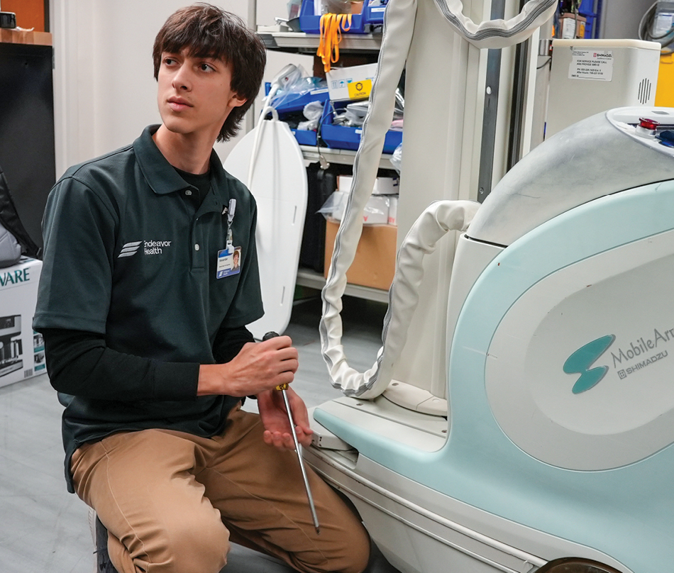 A student wearing a gray shirt and brown pants with a medical machine
