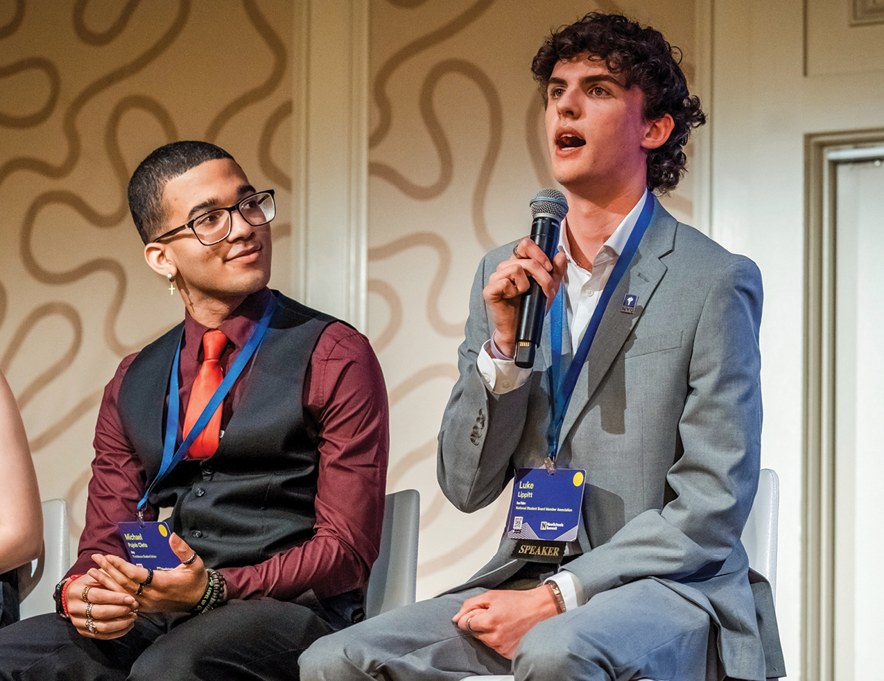 Two teens in suits sit on a panel with microphones