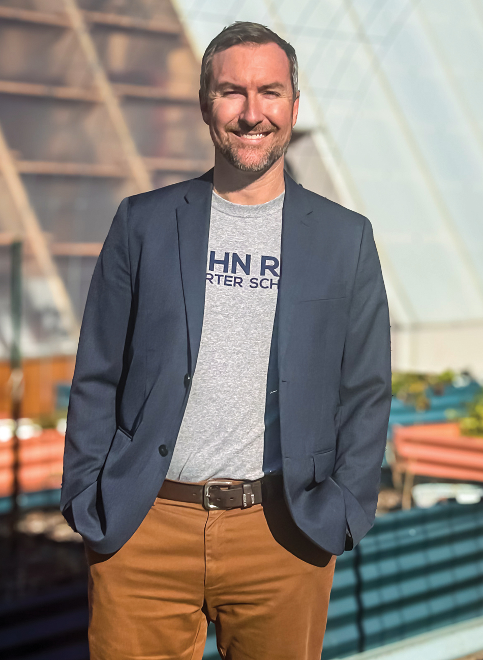 A man standing in front of gardening area in suit jacket and brown pants