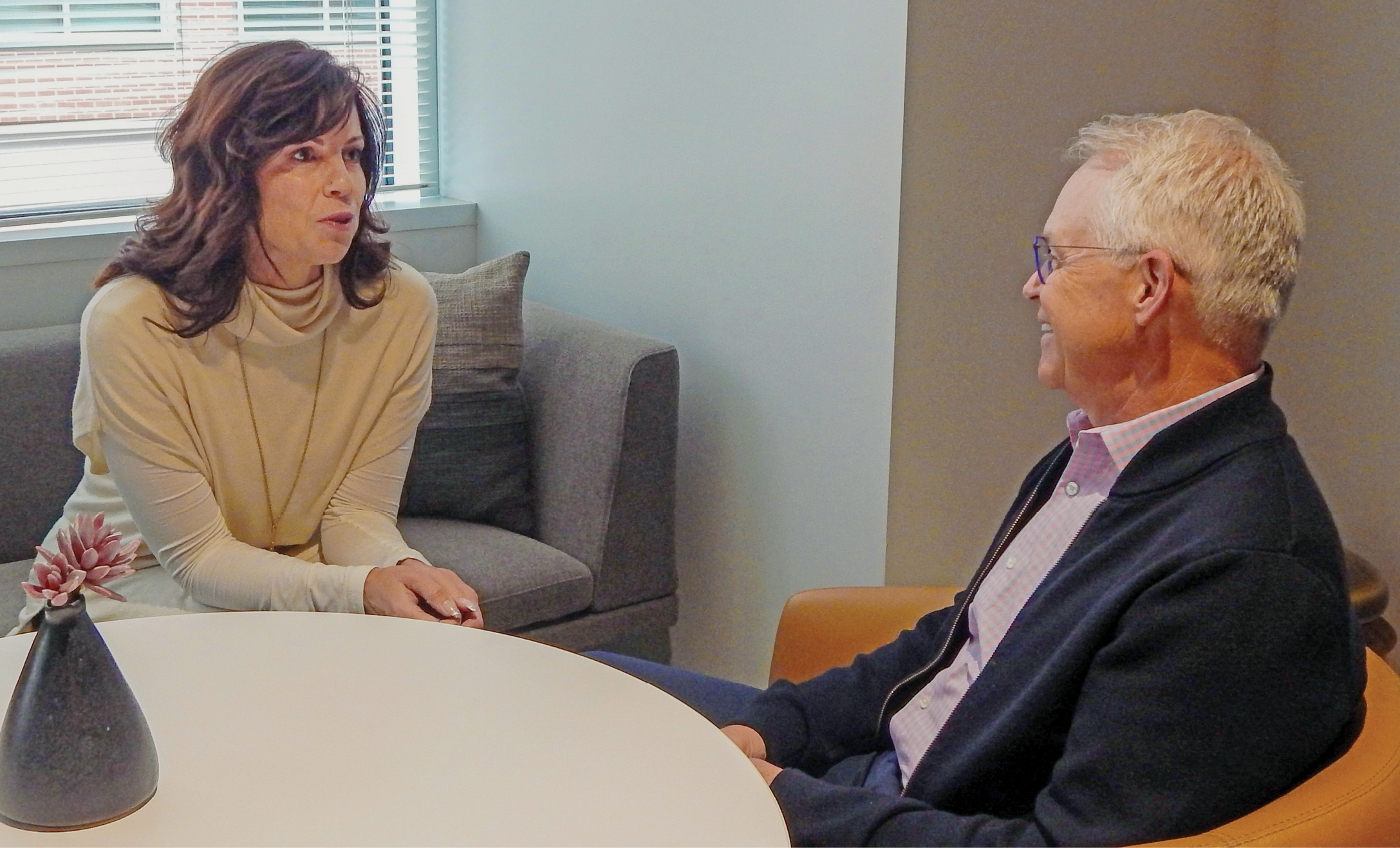 A brunette white woman and a white man with gray hair sit and talk at a table