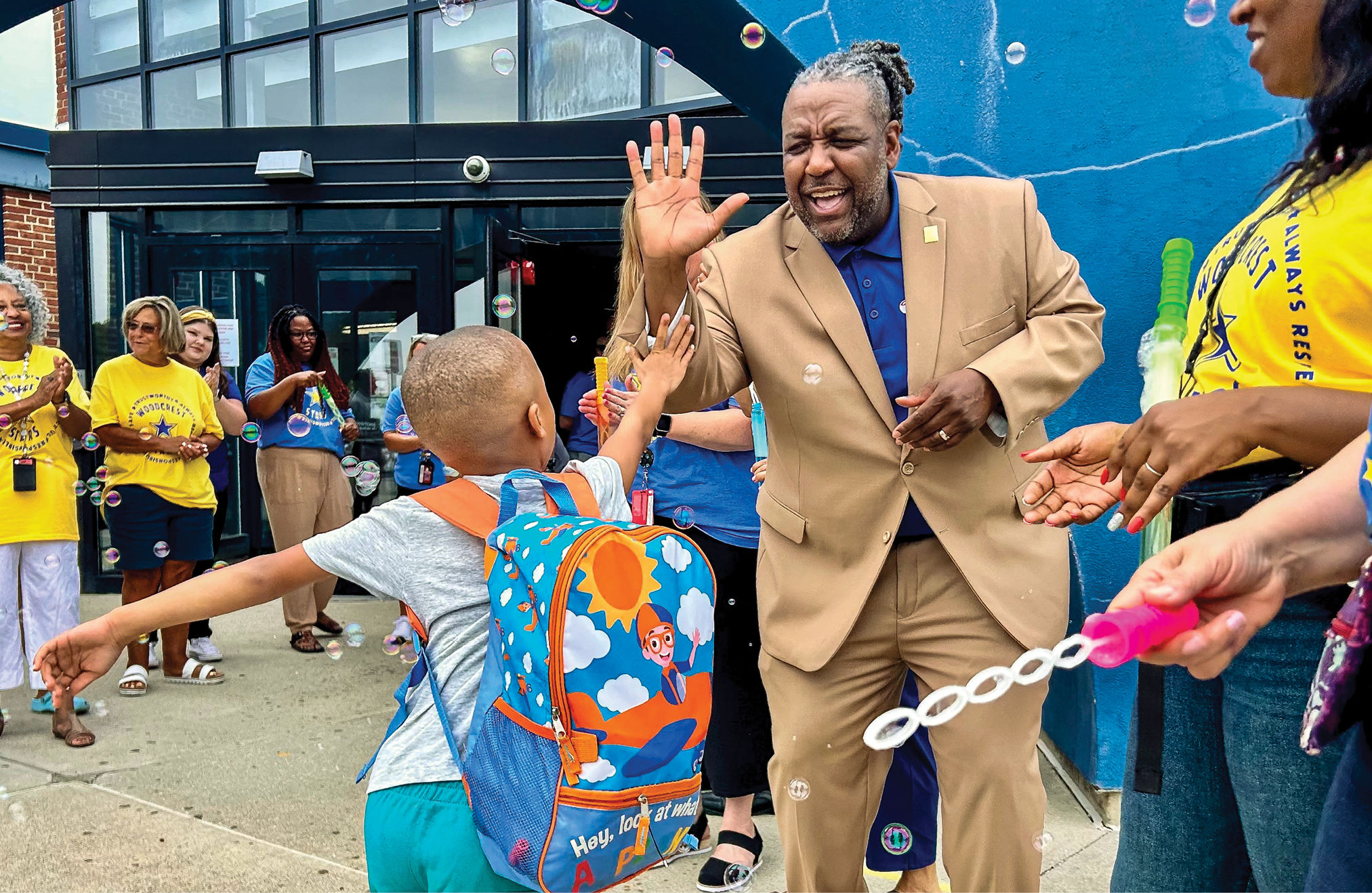 A Black man wearing a suit high fiving a kid with a backpack