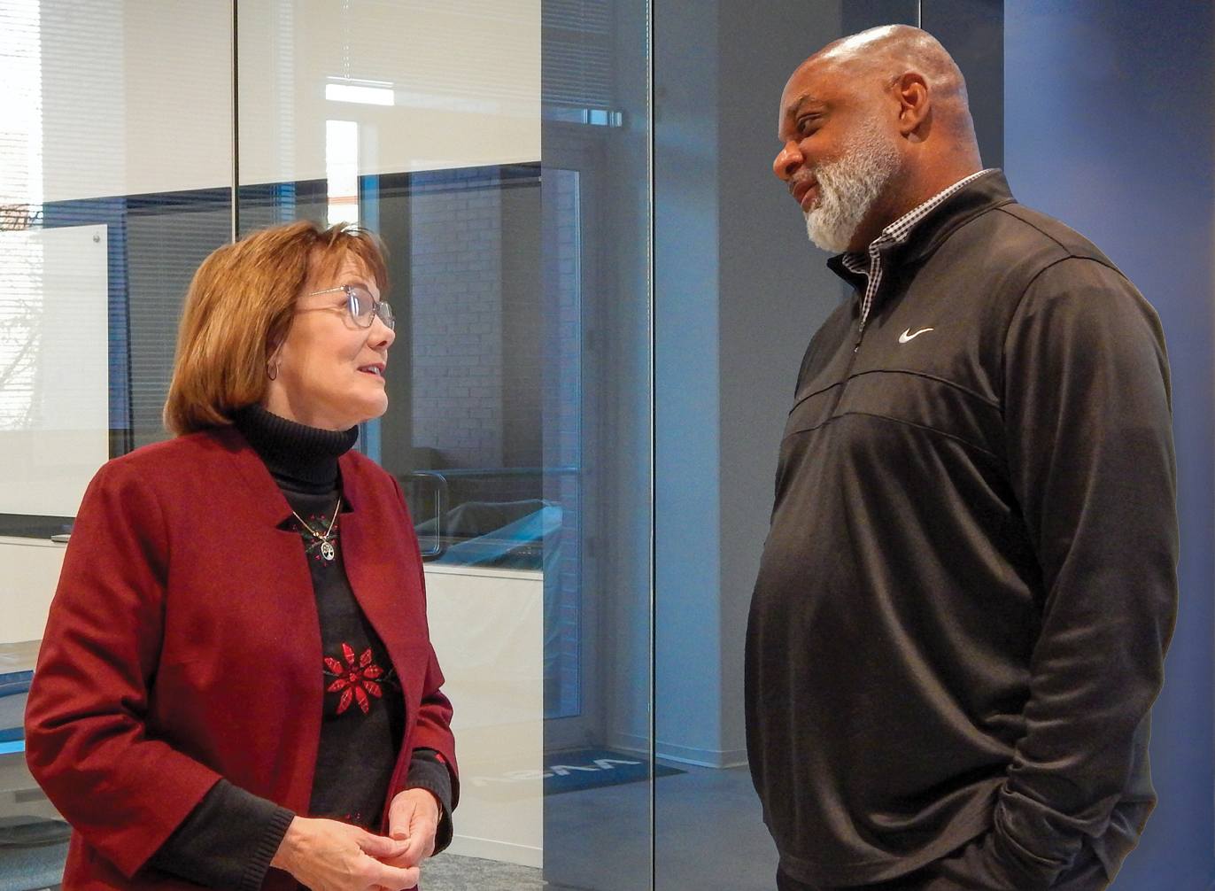 A white woman and a Black man talking in an office with glass doors
