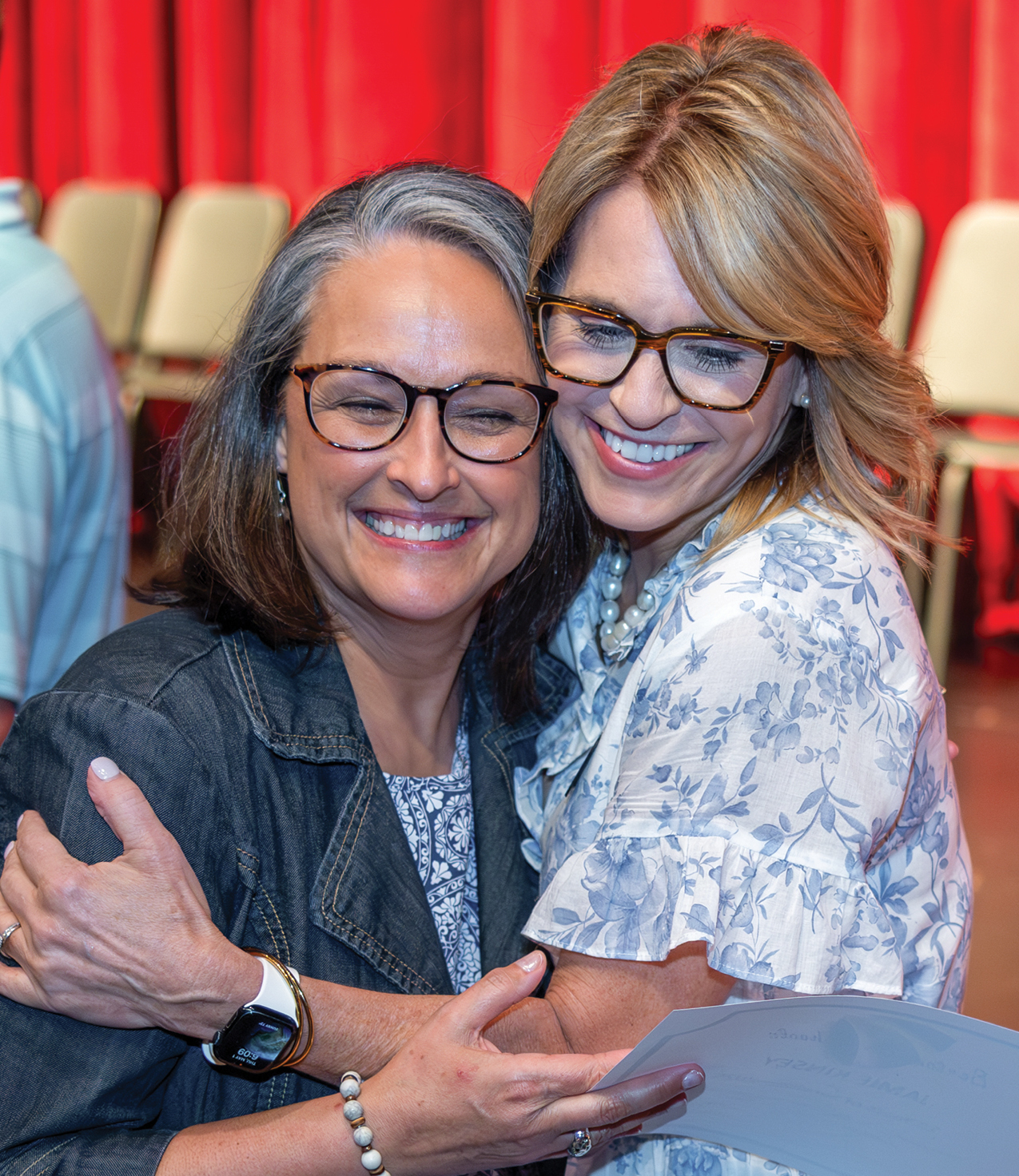 Two women wearing glasses hugging and smiling