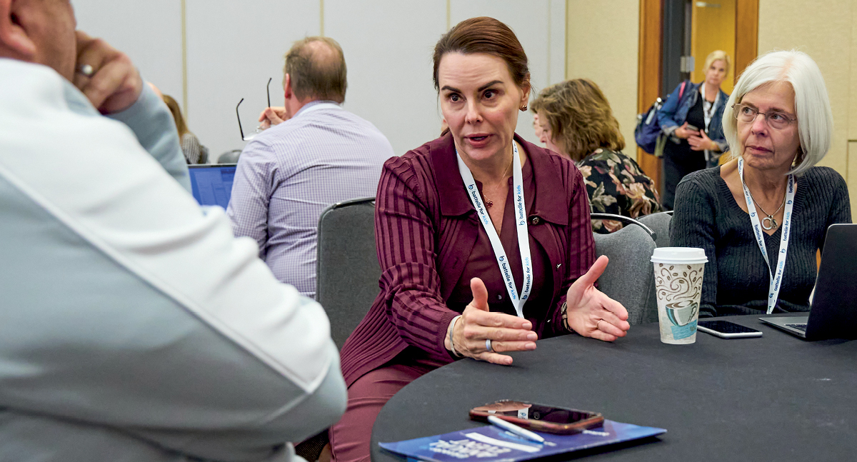 A woman in a plum blazer sitting at table discussing with other people s